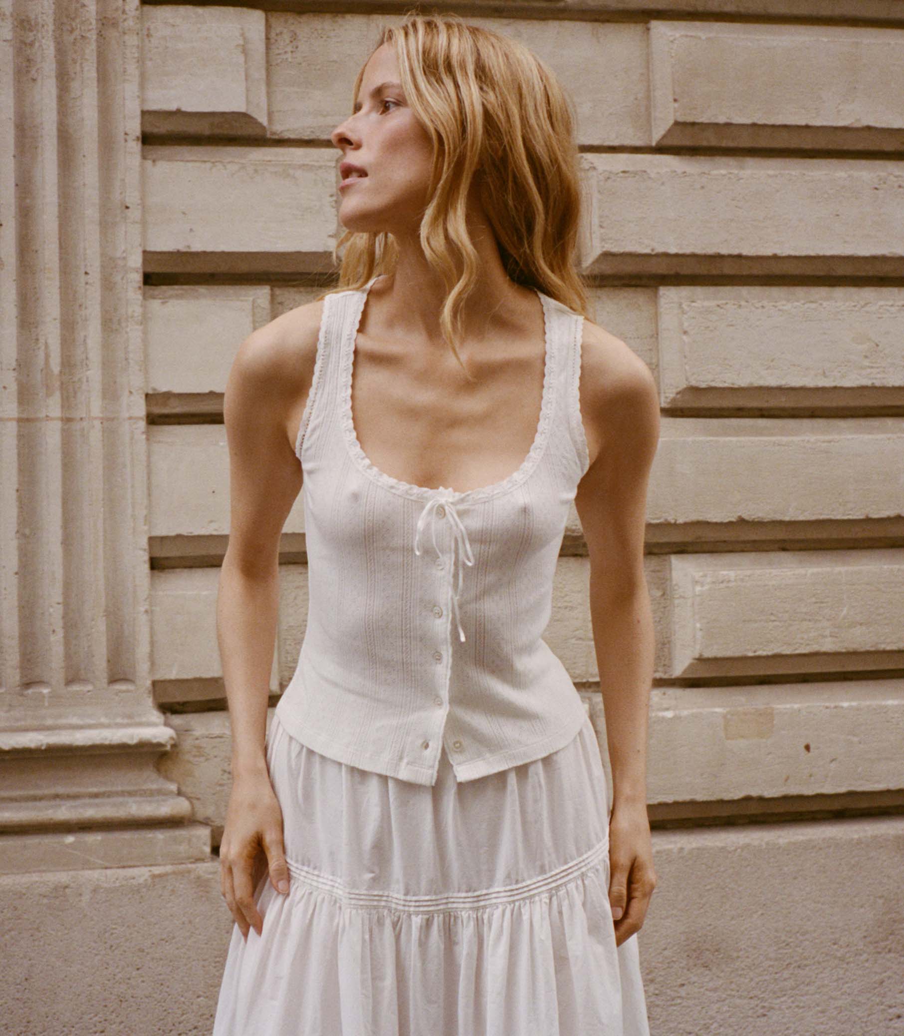 Stylish model wearing a white top from the Tees collection against a classic architectural backdrop.
