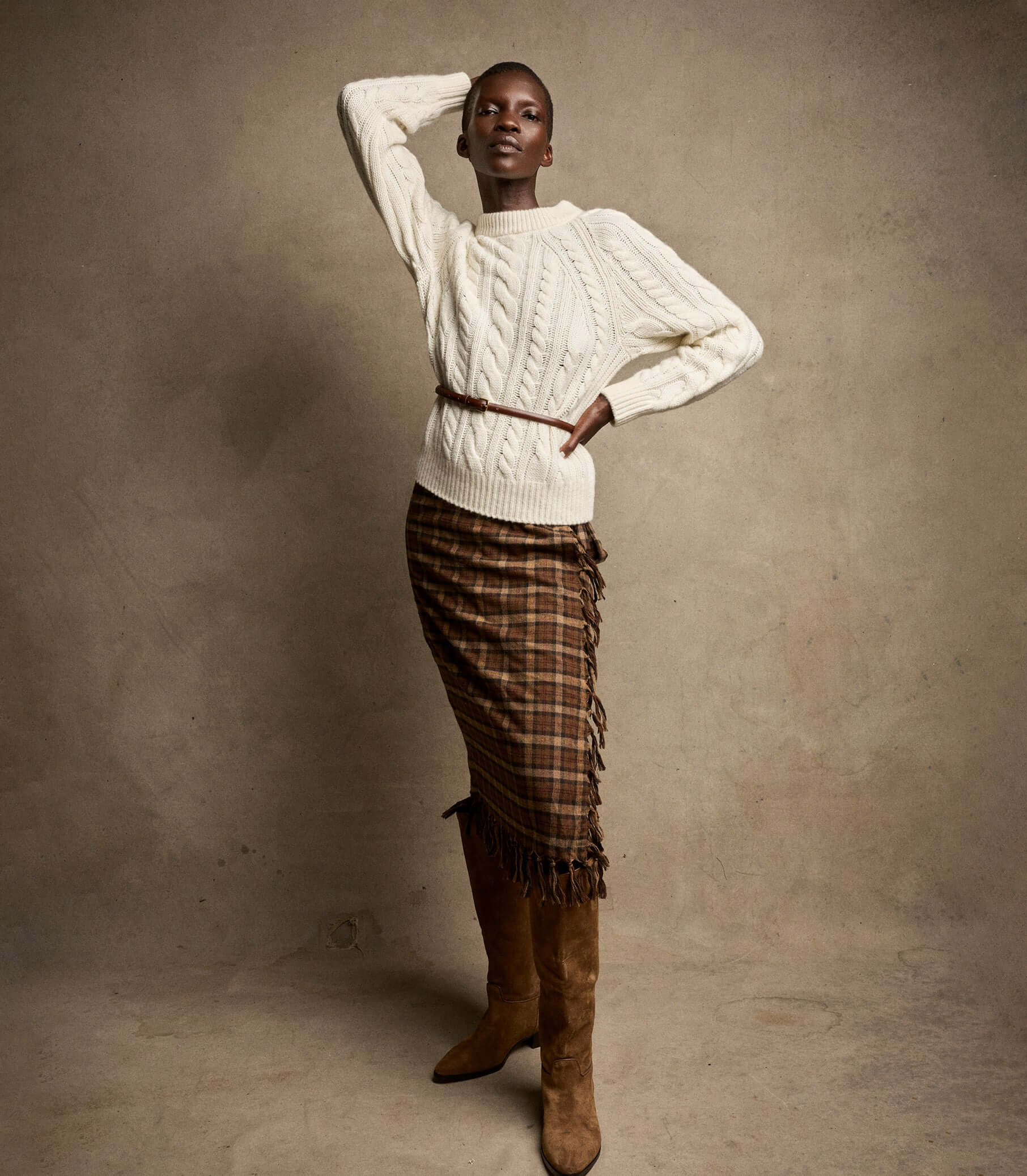 Model wearing stylish Knitwear, a cozy cable-knit sweater paired with a plaid skirt and knee-high boots.